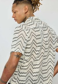 Chemise à manches courtes avec un motif en zigzag blanc et noir, dotée d'un col boutonné et d'un tissu texturé. Détails Intriqués tout au long.