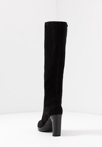 Stivale alto in suede nero, con punta arrotondata, dettagli di cuciture verticali e tacco robusto. Superficie liscia, hardware minimale.