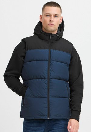 Wattierte Weste in Marineblau mit einer schwarzen Kapuze und Ärmel. Verfügt über einen Reißverschluss vorne, ein gestepptes Design und zwei Seitentaschen. Strukturierter Stoff.