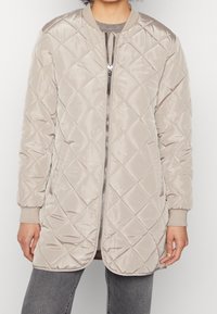 Kvadramönstrad beigemelerad bomberjacka med dragkedja fram, ribbade ärmar och en slät yta. Har diamantmönster och en avslappnad silhuett.