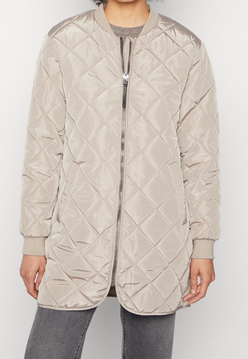 Kvadramönstrad beigemelerad bomberjacka med dragkedja fram, ribbade ärmar och en slät yta. Har diamantmönster och en avslappnad silhuett.