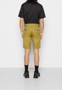 Khaki šortky se rovnou siluetou, zadními kapsami a poutky na opasek, v kombinaci s černým tričkem s krátkým rukávem a černými teniskami.