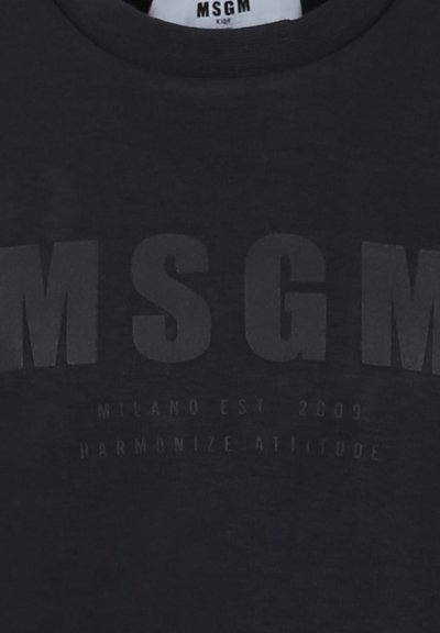 T-shirt grigio scuro con collo tondo. Presenta una scritta nera in rilievo in bold con le parole "MSGM", "MILANO EST 2009" e "HARMONIZE ATTITUDE."