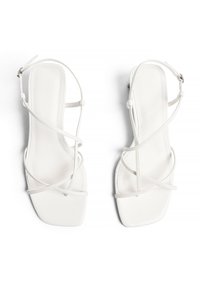 Weiße Riemchensandalen mit quadrater Zehenpartie und flachem Absatz. Sie verfügen über dünne Riemen mit einer verstellbaren Schnalle am Knöchel und sind aus glattem synthetischem Material gefertigt.