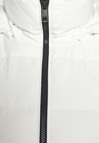 Vit puffjacka med hög krage och dragkedja framtill med svart dragkedja. Slät yta med quiltade sektioner och diskret varumärkesdetalj.