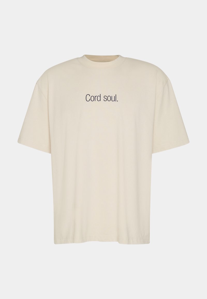 T-shirt surdimensionné de couleur crème en coton doux, avec le texte « Cord soul. » imprimé en bleu foncé sur le devant.