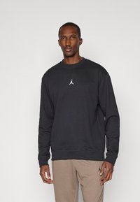 Schwarzes Sweatshirt mit langen Ärmeln, Rundhalsausschnitt und gerippten Bündchen. In der Mitte befindet sich ein weißes Jumpman-Logo. Weicher Stoff.