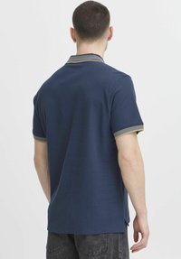 Marineblå polo med ribbad krage i beige detaljer och korta ärmar, tillverkad av ett mjukt, strukturerat tyg. Sidoslitsar för bättre passform.