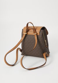 Sac à dos marron à motifs avec des accents en cuir beige, une poignée supérieure, des bretelles réglables et une poche zippée pour un rangement sécurisé.