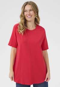 T-shirt rosso a maniche corte realizzato in tessuto morbido, con scollo rotondo e vestibilità rilassata, abbinato a jeans in denim blu.