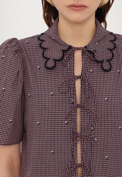 Kortermet, rutete bluse i svart og rosa med en bølget krage, frontknuter og små broderte detaljer.