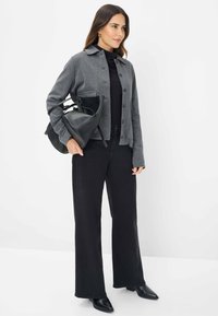 Giacca grigia intrecciata con bottoni, dolcevita nera, jeans neri a vita alta e borsa nera, completando un look contemporaneo.