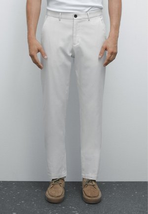 Light gray trousers made of smooth fabric, featuring a button closure, front pockets, and a tapered fit. Paired with brown suede shoes.