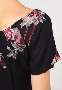 Haut en tissu noir avec des motifs floraux en bourgogne et gris, doté d'un décolleté large et de manches courtes, affichant une texture lisse.