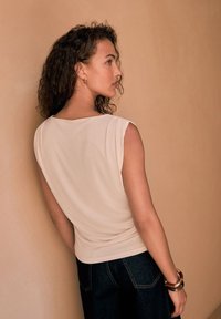 Top senza maniche di un beige chiaro con una vestibilità comoda, texture morbida e scollatura rotonda, abbinato a jeans in denim scuro. Design semplice, senza motivi o logo.
