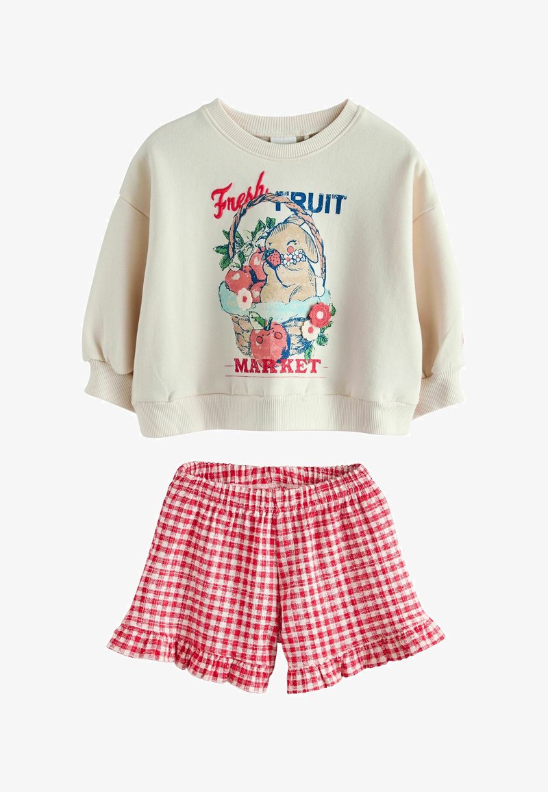 Krema majica s voćnom košaricom i natpisom "Svježe voće na tržištu", u kombinaciji s crveno-bijelim kariranim kratkim hlačama s volanima.