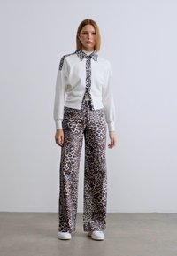 Λευκό πουλόβερ με λεπτομέρειες σε σχέδιο ζώου, σε συνδυασμό με παντελόνι με φαρδιά μπατζάκια που φέρει παρόμοιο σχέδιο λεοπάρ σε καφέ και εκρού. Άσπρα παπούτσια.