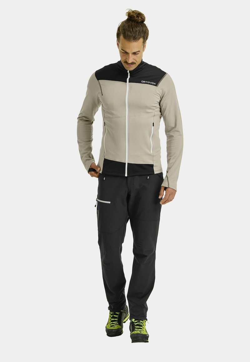 Light gray and black jacket with a zip front, featuring a high collar and two side pockets, worn with black pants and hiking boots.