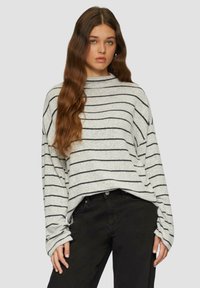 Lichtgrijze gestreepte trui met zwarte horizontale lijnen, losse pasvorm, hoge hals en lange mouwen, gecombineerd met zwarte broek.