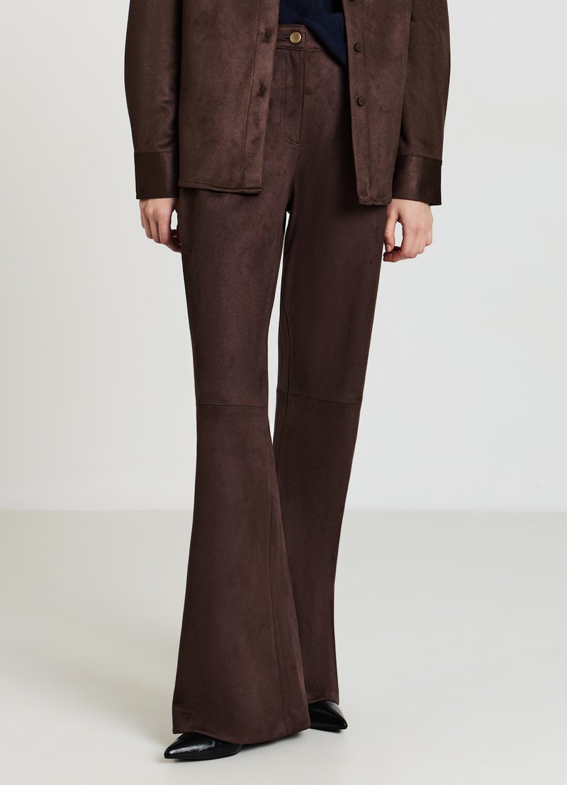 Braune Schlaghosen aus weichem, wildlederähnlichem Material mit glatter Textur. Kombiniert mit einer passenden, geknöpften Jacke und spitzen schwarzen Schuhen.