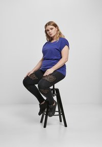 Fialové tričko s krátkym rukávom v kombinácii s čiernymi legínami, ktoré majú leopardí potlač z jemnej sieťoviny na kolenách, nosené s čiernymi teniskami.