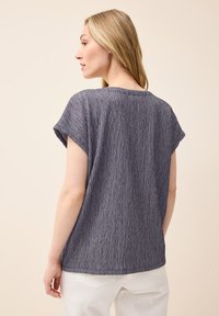 Top de color navy con textura, de mangas cortas, cuello redondo y un corte relajado. Presenta un sutil patrón acanalado y cuelga de forma holgada del cuerpo.