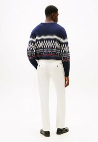Suéter de punto azul marino con patrones geométricos en blanco y rojo; combinado con pantalones blancos y zapatos negros, visto desde la parte de atrás.