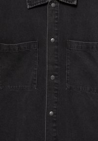 Fekete denim ing klasszikus gallérral, középső gombos záródással és két pattentolt zsebbel. A textúra sima, finom varrási részletekkel.