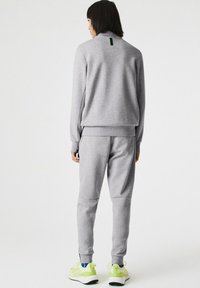 Sudadera gris y pantalones a juego de tela suave. Presenta un pequeño acento verde en el cuello. Calzado: zapatillas amarillas claras.