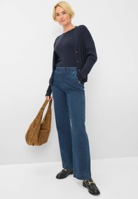 Marineblauw ribgebreid langemouwen top, open voorzijde gebreide cardigan, wijde blauwe denim broek, bruine suède tas met studs, zwarte loafers.