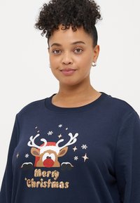 Tmavomodrá mikina vyrobená z bavlny, s grafickým motívom soba so Santa klobúkom a flitrami s textom "Veselé Vianoce". Dizajn s okrúhlym výstrihom.