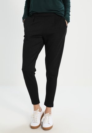 Zwarte op maat gemaakte broek met zijzakken, voorzien van een gladde stoftextuur en een slim fit, gecombineerd met witte sneakers.