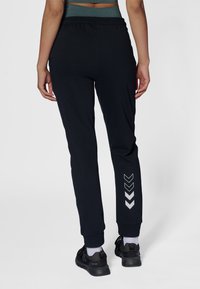 Czarne spodnie sportowe o zwężanym kroju, z elastycznym pasem i odblaskowym wzorem w kształcie szewronu na dole nogawki. Gładka tekstura materiału.