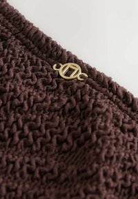 Bruin gestructureerde stof met een geweven patroon en een gouden metalen sluiting, met een close-up van het materiaal en de designelementen.