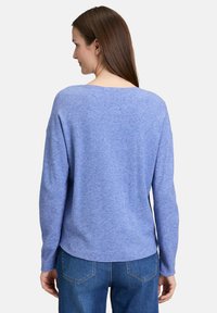 Pull-over en tricot bleu avec un large col et des manches longues. Ourlet légèrement arrondi et texture douce. Porté avec un jean bleu.