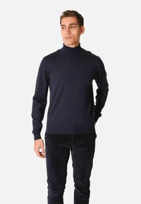 Maglione dolcevita navy in morbido tessuto a maglia, con maniche lunghe, polsini e orlo a coste, abbinato a pantaloni in velluto a coste scuri.
