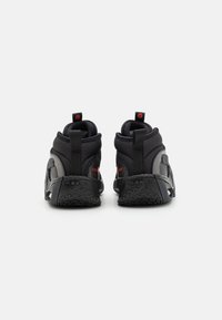 Czarne sportowe buty z wysoką cholewką, teksturowaną górą, kontrastującymi szarymi panelami i czerwonymi akcentami. Posiadają pętelki na pięcie.