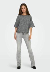 Sivi pleteni top s širokim rukavima, uparen s svijetlosivim trapericama s širim nogavicama. Outfit ima opušteni kroj i minimalistički dizajn.