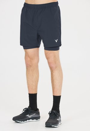 Mand iført sorte atletikshorts med indbyggede kompressionsshorts, sorte sokker og sorte løbesko på hvid baggrund.