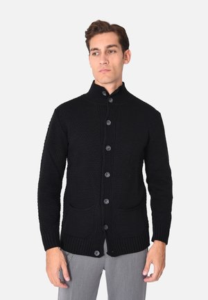 Cardigan lavorato a maglia nero con colletto alto, chiusura frontale a bottoni e due tasche anteriori. La texture è spessa, con polsini e orlo a coste.