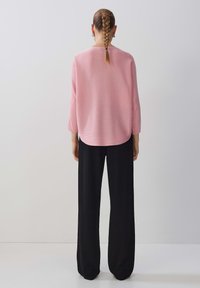 Haut en tricot creux rayé rose pâle à manches trois-quarts, associé à un pantalon large noir. Texture lisse et ourlet arrondi.