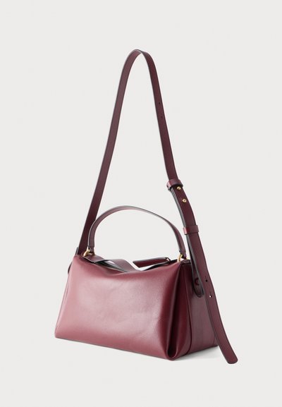 Ορθογώνια τσάντα χειρός από δέρμα μπορντό με επάνω λαβή και ρυθμιζόμενο μακρύ λουρί ώμου, τοποθετημένη μπροστά σε απλό φόντο.