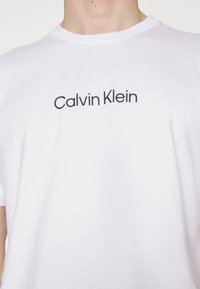 Witte katoenen t-shirt met zwarte "Calvin Klein" tekst op de borst. Korte mouwen en een ronde halslijn, gladde textuur.