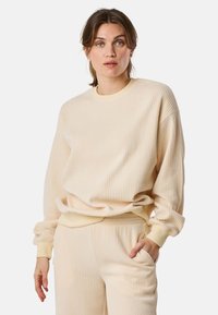 Beige geribde sweatshirt met lange mouwen, ronde hals en een relaxed fit. Het materiaal lijkt zacht en textuur te hebben, wat visuele interesse creëert.