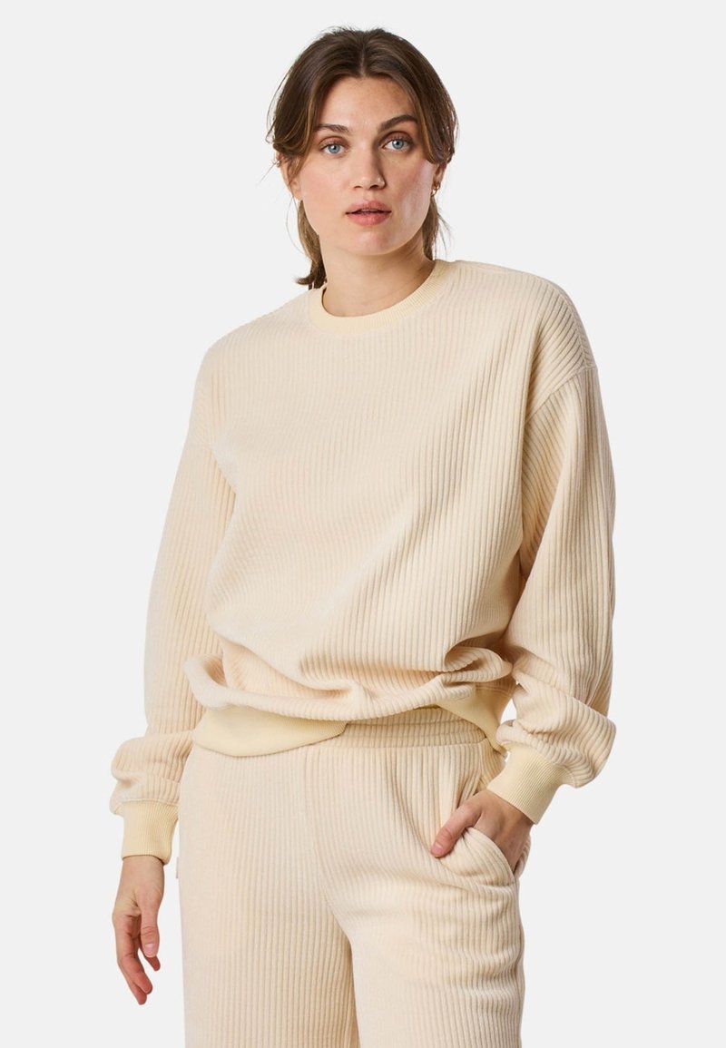Beige geribde sweatshirt met lange mouwen, ronde hals en een relaxed fit. Het materiaal lijkt zacht en textuur te hebben, wat visuele interesse creëert.
