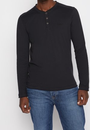 Zwarte lange mouw shirt met een henley halslijn, drie knopen en een aangesloten ontwerp. Gecombineerd met blauwe spijkerbroeken, wat een casual stijl en comfort uitstraalt.