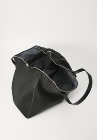 Sac fourre-tout noir en nylon avec une grande ouverture, deux poignées, des détails en zip doré et un intérieur lisse et doublé.