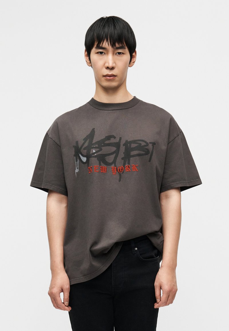 Σκούρο γκρι υπερμεγέθες βαμβακερό μπλουζάκι, με  έντονο μαύρο και κόκκινο γραφικό κείμενο στο εμπρός μέρος. Κοντά μανίκια και στρογγυλή λαιμόκοψη.