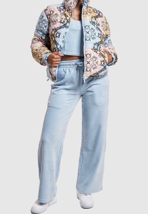 Personne portant une doudoune à motifs patchwork pastel, un crop top côtelé bleu clair, un pantalon large assorti et des baskets blanches.