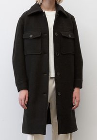 Cappotto in lana nera con vestibilità su misura, caratterizzato da un colletto a punte, due tasche frontali e chiusura a bottone. Tessuto liscio, design lungo fino al ginocchio.